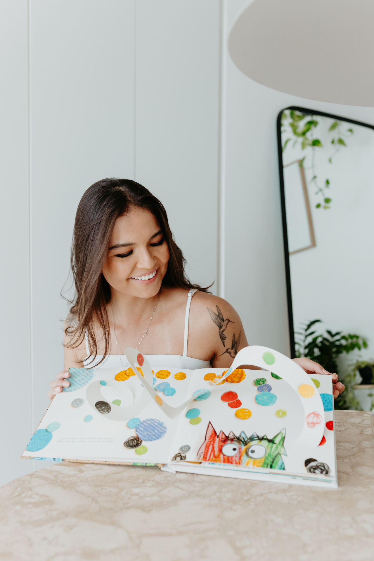 Kamila Tsuru trabalhando com livros, cartas e materiais terapêuticos sobre uma mesa clara.